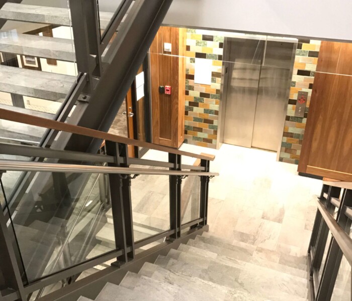 A commercial building with interior glass railings with a wooden cap and stainless steel assist rail.
