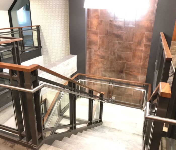 A downward view of commercial interior glass railings with stainless steel handrail and wooden cap.